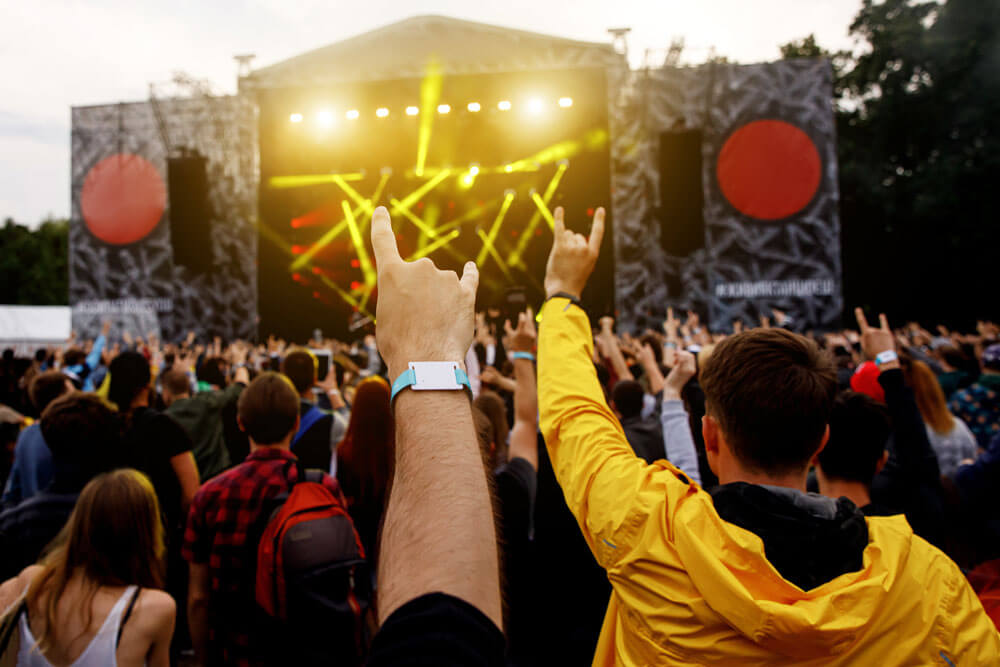 Attendees at a concert hold up "rock" gestures with custom wristbands visible on their arms